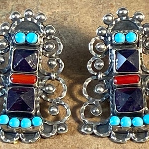May include: A pair of silver earrings with a geometric design. The earrings feature turquoise, amethyst, and coral stones.