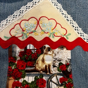 May include: A denim tote bag with a red scalloped trim and a white lace overlay. The bag features an embroidered design of hearts and flowers, and a patch with a cat and red flowers.