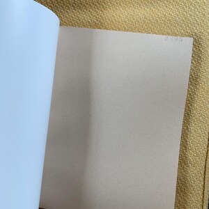 May include: Open book with white and light tan pages. The left side of the book shows the white pages, while the right side displays a light tan page. The book is open on a yellow textured surface.