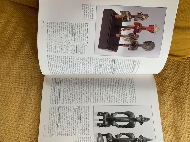 May include: A page from a book featuring images of African art. The top image displays several carved wooden figures on a black stand. The figures are in various colors, including red, brown, and white. The page also contains text.