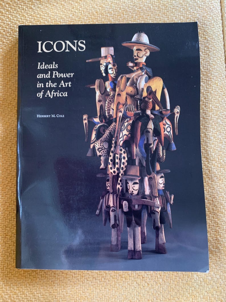 May include: A book titled "ICONS" with the subtitle "Ideals and Power in the Art of Africa" by Herbert M. Cole. The cover features a dark background and a sculpture composed of several carved wooden figures in various colors.