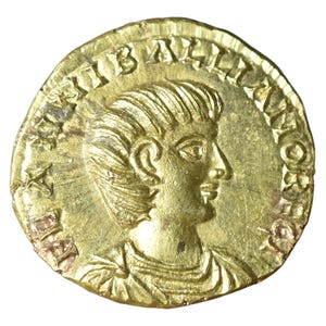 May include: A gold coin featuring a profile of a person with detailed hair and a laurel wreath. The coin has inscriptions around the edge and is set against a white background. The coin's surface shows signs of wear.
