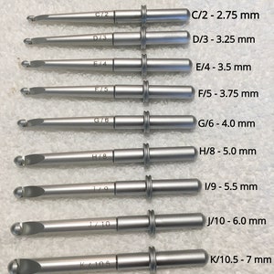 May include: A set of ten silver crochet hooks with different sizes labeled C/2 - 2.75 mm, D/3 - 3.25 mm, E/4 - 3.5 mm, F/5 - 3.75 mm, G/6 - 4.0 mm, H/8 - 5.0 mm, I/9 - 5.5 mm, J/10 - 6.0 mm, K/10.5 - 7 mm.