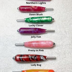 May include: Seven cylindrical handles with silver-toned metal ends, each featuring a unique marbled resin pattern. The text labels are Northern Lights, Dawn Blush, Lucky Clover, Jelly Fish, Pretty in Pink, Lady Bug, Orange Macaw, and All handles are the same size.