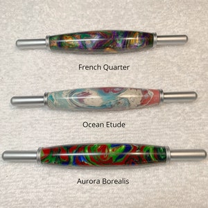 May include: Three wooden knitting needles with silver metal tips. The needles are decorated with colorful marbled patterns. The needles are labeled "French Quarter", "Ocean Etude", and "Aurora Borealis".