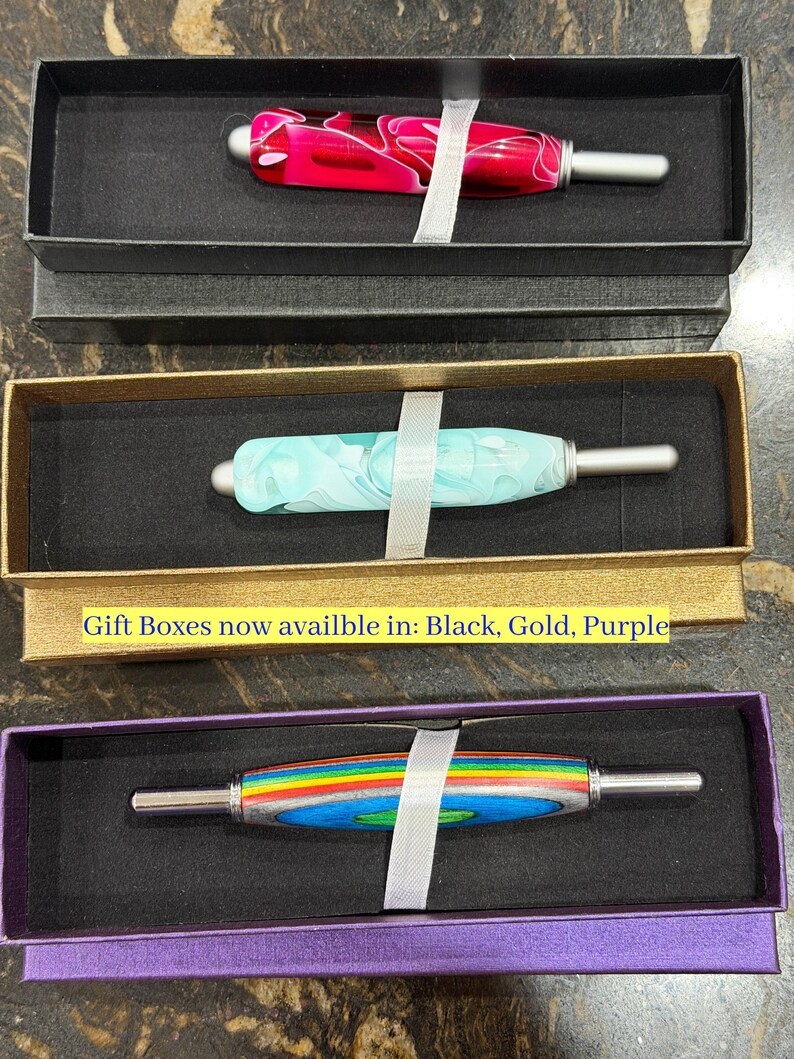 May include: Three seam rippers with decorative handles in black, gold, and purple gift boxes. The top handle is pink and white swirl, the middle is light blue and white swirl, and the bottom is rainbow striped. Text reads: Gift Boxes now availble in: Black, Gold, Purple.