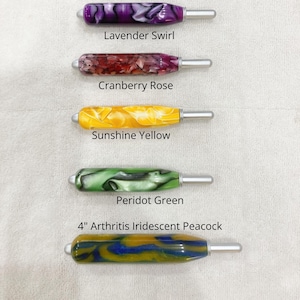 May include: Five crochet hooks with thick, ergonomic, marbled resin handles in various colors. The labels read Lavender Swirl, Cranberry Rose, Sunshine Yellow, Peridot Green, and 4" Arthritis Iridescent Peacock, each featuring a silver metal hook tip.