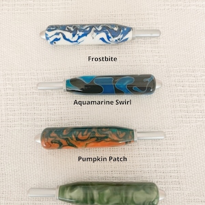 May include: Four crochet hook handles with metallic tips, labeled Frostbite in blue and white, Aquamarine Swirl in black and blue, Pumpkin Patch in orange and green, and Green Jade in solid green. Text states: All crochet handles are the same size.