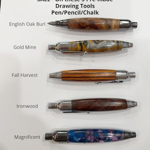 May include: Five drawing tools with chrome hardware and distinct barrels labeled English Oak Burl, Gold Mine, Fall Harvest, Ironwood, and Magnificent. The text reads: SALE - On these 5 Pre-made Drawing Tools Pen/Pencil/Chalk. Each tool has a unique finish.