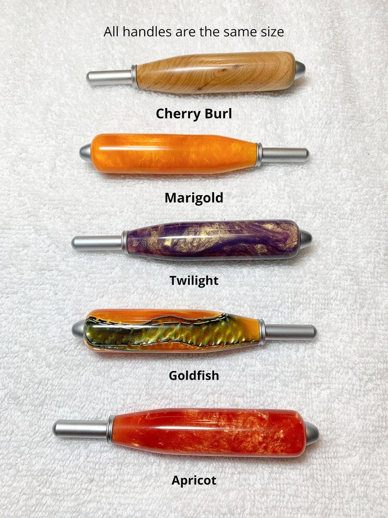 May include: Five crochet hook handles with silver metal tips, arranged vertically. The handles are labeled: Cherry Burl, Marigold, Twilight, Goldfish, and Apricot. Text at the top states: All handles are the same size. Each handle features a unique color and pattern, including wood grain, solid orange, purple and gold swirl, textured green and orange, and marbled red.