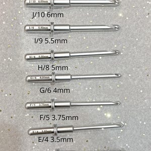 May include: A set of silver crochet hooks with different sizes labeled in millimeters. The hooks are arranged from largest to smallest. The text "In-Line Crochet Hooks" is at the top of the image. The text "All hooks are compatible with my existing and previous crochet handles" is at the bottom of the image.