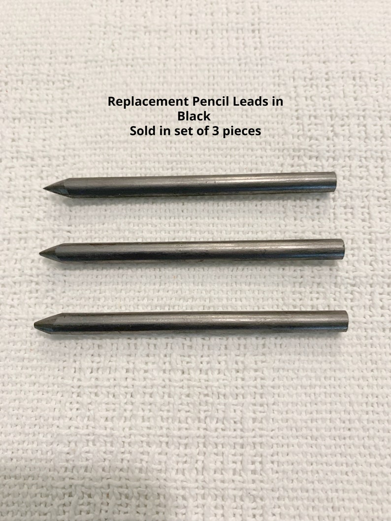 May include: Three black replacement pencil leads arranged horizontally. The text above the leads reads: Replacement Pencil Leads in Black. Sold in set of 3 pieces. Each lead is cylindrical with a pointed tip and a flat end.