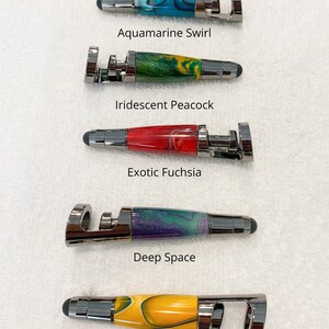 May include: Six phone stands with different colored wooden inlays. The stands are all the same size and have a metal ring on the top. The colors of the inlays are aquamarine swirl, iridescent peacock, exotic fuchsia, deep space, and sunflower yellow.