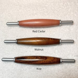 May include: Three wooden seam rippers with silver metal ends. The top tool is labeled Red Cedar, the middle is Walnut, and the bottom is Koa. Each tool features a smooth, rounded wooden handle with a polished finish and silver metal ferrules.