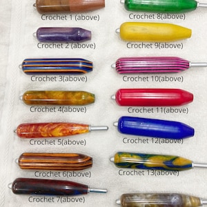May include: A collection of 14 crochet hooks with colorful, ergonomic handles. The handles are made of various materials and feature a variety of colors and patterns. Text on the image reads "My best sell ever on crochet handle and box of hooks!" and "They are arthritis crochet handle which are 4" long and thicker (except item 2 - standard length)"