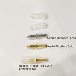 May include: An assortment of needle threaders in chrome and gold finishes, with protective caps. The image shows three threaders, one chrome and two gold, with the text "Needle Threader - Chrome", "Needle Threder - Gold", and "Needle Threder - Gold with protective cap".