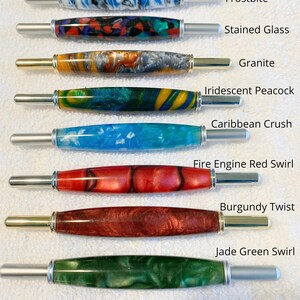May include: Ten seam rippers with colorful resin handles and metal ends. The handles feature patterns labeled Tequila Sunset, Frostbite, Stained Glass, Granite, Iridescent Peacock, Caribbean Crush, Fire Engine Red Swirl, Burgundy Twist, Jade Green Swirl, and Purple Galaxy.