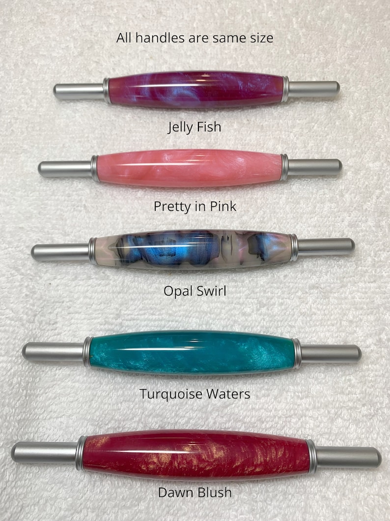 May include: Five cylindrical tools with metallic silver ends and polished resin barrels in various colors. The text reads: All handles are same size, Jelly Fish, Pretty in Pink, Opal Swirl, Turquoise Waters, and Dawn Blush. Each barrel features a unique marbled or pearlescent finish in shades of magenta, pink, blue, turquoise, and red with gold accents.