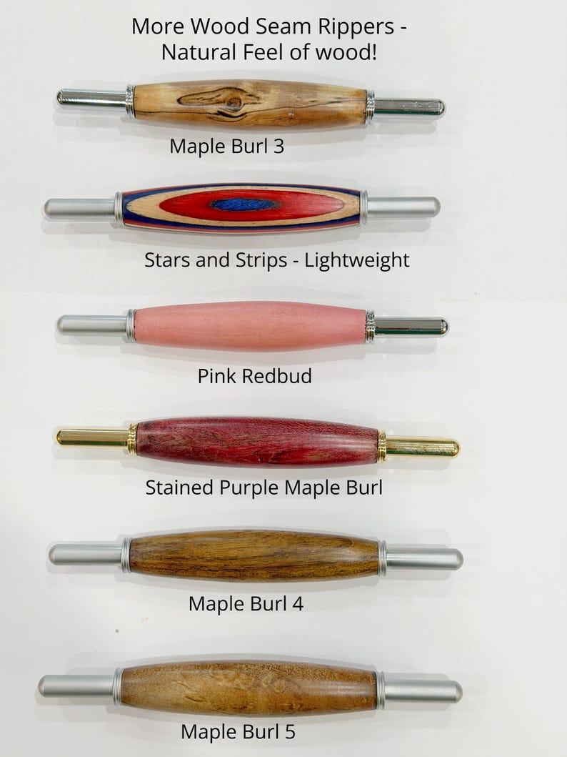 May include: Six seam rippers with wooden handles arranged vertically. The handles are labeled: Maple Burl 3, Stars and Strips, Pink Redbud, Stained Purple Maple Burl, Maple Burl 4, and Maple Burl 5. The metal tips are silver or gold colored.