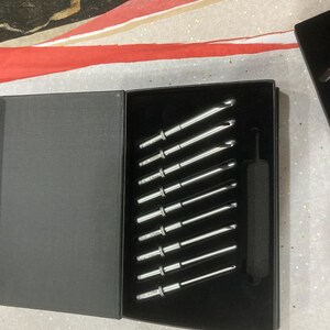 May include: A set of ten silver crochet hooks in a black box with a black velvet interior. The hooks are arranged in a diagonal line.