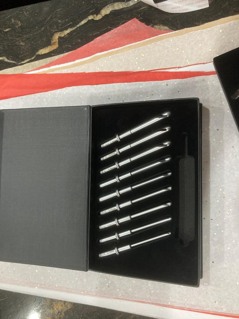 May include: A set of ten silver crochet hooks in a black box with a black velvet interior. The hooks are arranged in a diagonal line.