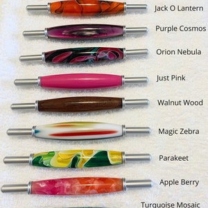 May include: Ten different colored pens with silver caps and metal tips. The pens are arranged vertically with the caps facing the right side of the image. The pens are labeled with names such as "Groovy Garnet", "Jack O Lantern", "Purple Cosmos", "Orion Nebula", "Just Pink", "Walnut Wood", "Magic Zebra", "Parakeet", "Apple Berry", and "Turquoise Mosaic".
