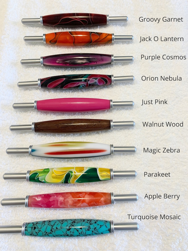 May include: Ten different colored pens with silver caps and metal tips. The pens are arranged vertically with the caps facing the right side of the image. The pens are labeled with names such as "Groovy Garnet", "Jack O Lantern", "Purple Cosmos", "Orion Nebula", "Just Pink", "Walnut Wood", "Magic Zebra", "Parakeet", "Apple Berry", and "Turquoise Mosaic".