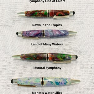 May include: Four pens from the Symphony Line of Colors, each with a unique marbled resin barrel and gold-tone accents. The pens are labeled Dawn in the Tropics, Land of Many Waters, Pastoral Symphony, and Monet's Water Lilies. All pens are the same size.