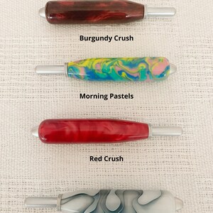 May include: Four crochet hooks with thick, polished handles in Burgundy Crush, Morning Pastels, Red Crush, and Pearl Swirl patterns. Each handle features a metallic silver tip and base. Text reads: All crochet handles are the same size.