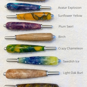 May include: Nine crochet hook handles arranged vertically, each with a unique finish: Dark Oak Burl, Avatar Explosion, Sunflower Yellow, Plum Swirl, Birch, Crazy Chameleon, Swedish Ice, Light Oak Burl, and Viking Storm. Each handle features a silver metal tip.