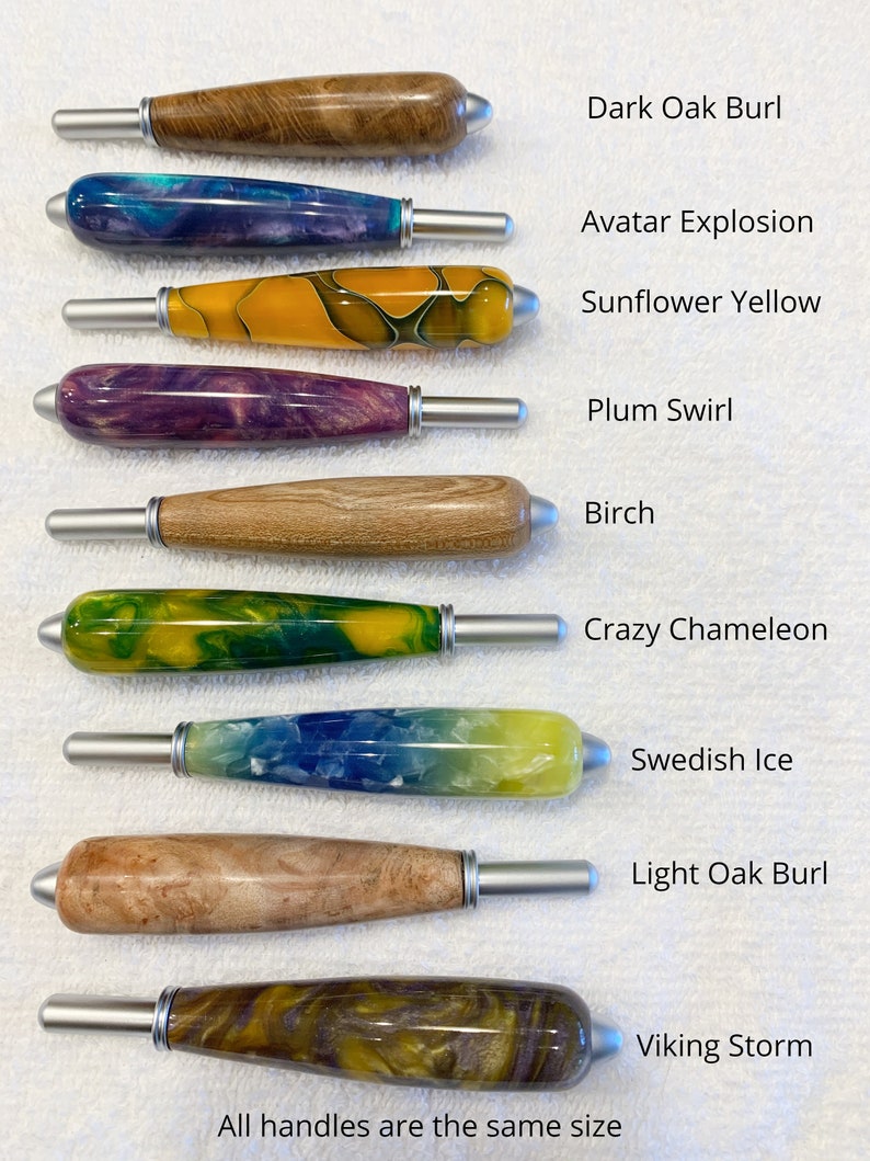 May include: Nine crochet hook handles arranged vertically, each with a unique finish: Dark Oak Burl, Avatar Explosion, Sunflower Yellow, Plum Swirl, Birch, Crazy Chameleon, Swedish Ice, Light Oak Burl, and Viking Storm. Each handle features a silver metal tip.