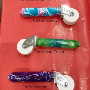 May include: Three seam rollers with white wheels and silver metal hardware. The handles are colorful: Cotton Candy (blue and pink), Carribean Crush (green), and Frozen Water (purple). Text: Seam Roller - Handier than you think!