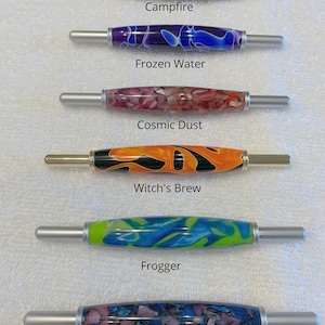 May include: Six different colorful crochet hooks with silver handles. The hooks are labeled "Campfire", "Frozen Water", "Cosmic Dust", "Witch's Brew", "Frogger", and "Maleficent". All 2 in 1 Tools Same Size.