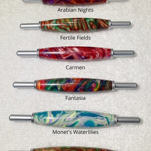 May include: Six different crochet hooks with colorful, marbled handles. The handles are labeled with names like "Arabian Nights", "Fertile Fields", "Carmen", "Fantasia", "Monet's Waterlilies", and "Dawn in the Tropics".