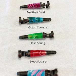 May include: Five different colored stylus pens with metal tops and bottoms. The pens are arranged vertically with the text "All Stands are Same Size" at the top and the names of each pen color below each pen. The names are "Amethyst Swirl", "Ocean Currents", "Irish Spring", "Exotic Fuchsia", and "Cotton Candy".