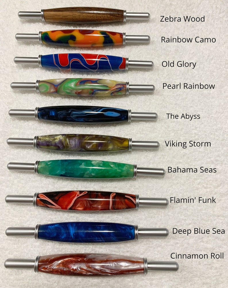 May include: Ten different wooden pens with various colorful patterns and designs. The pens are arranged vertically with the names of each pattern listed to the right of each pen. The names of the patterns are: Zebra Wood, Rainbow Camo, Old Glory, Pearl Rainbow, The Abyss, Viking Storm, Bahama Seas, Flamin' Funk, Deep Blue Sea, and Cinnamon Roll.