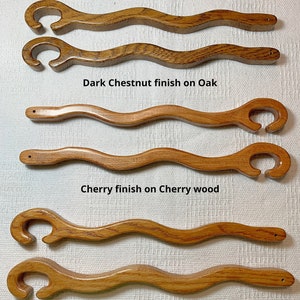May include: Four wooden oven rack hooks in different finishes: dark chestnut, cherry, and golden oak. The text "Oven Rack Hooks available in 3 finishes" is at the top of the image. The text "Dark Chestnut finish on Oak", "Cherry finish on Cherry wood", and "Golden Oak finish on Oak" are below each hook.