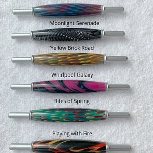 May include: Six wooden crochet hooks with colorful patterns and silver metal tips. The hooks are labeled with names like "Night Music", "Moonlight Serenade", "Yellow Brick Road", "Whirlpool Galaxy", "Rites of Spring", and "Playing with Fire".