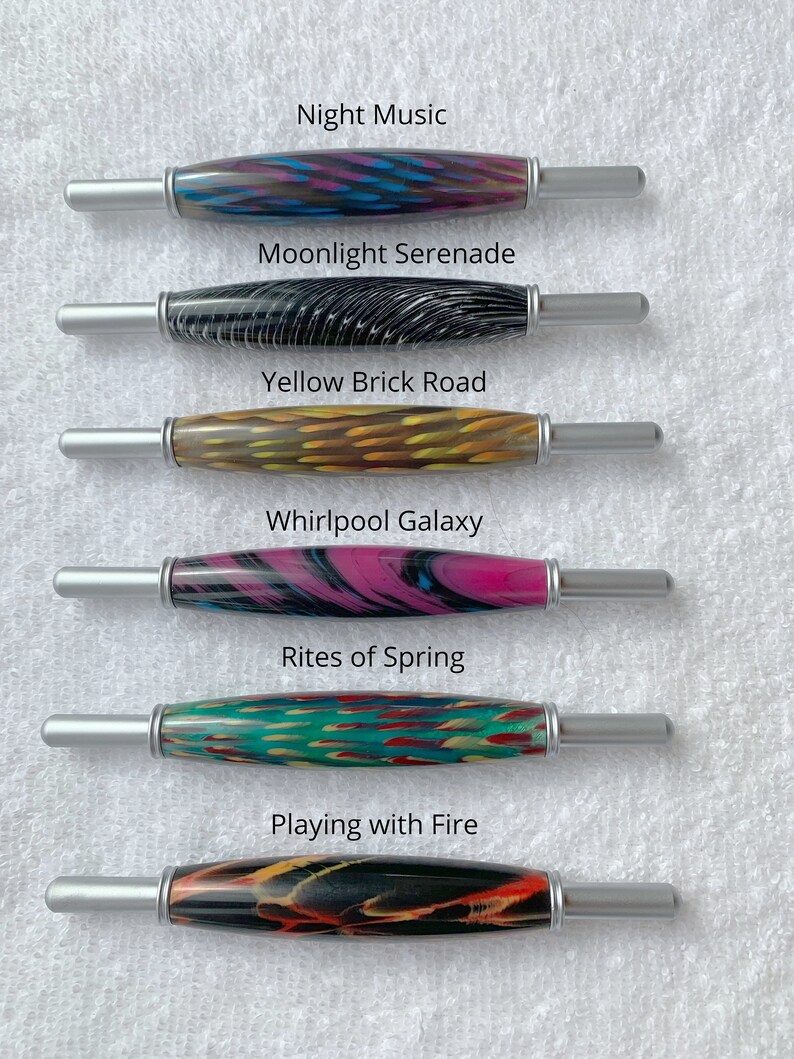 May include: Six wooden crochet hooks with colorful patterns and silver metal tips. The hooks are labeled with names like "Night Music", "Moonlight Serenade", "Yellow Brick Road", "Whirlpool Galaxy", "Rites of Spring", and "Playing with Fire".
