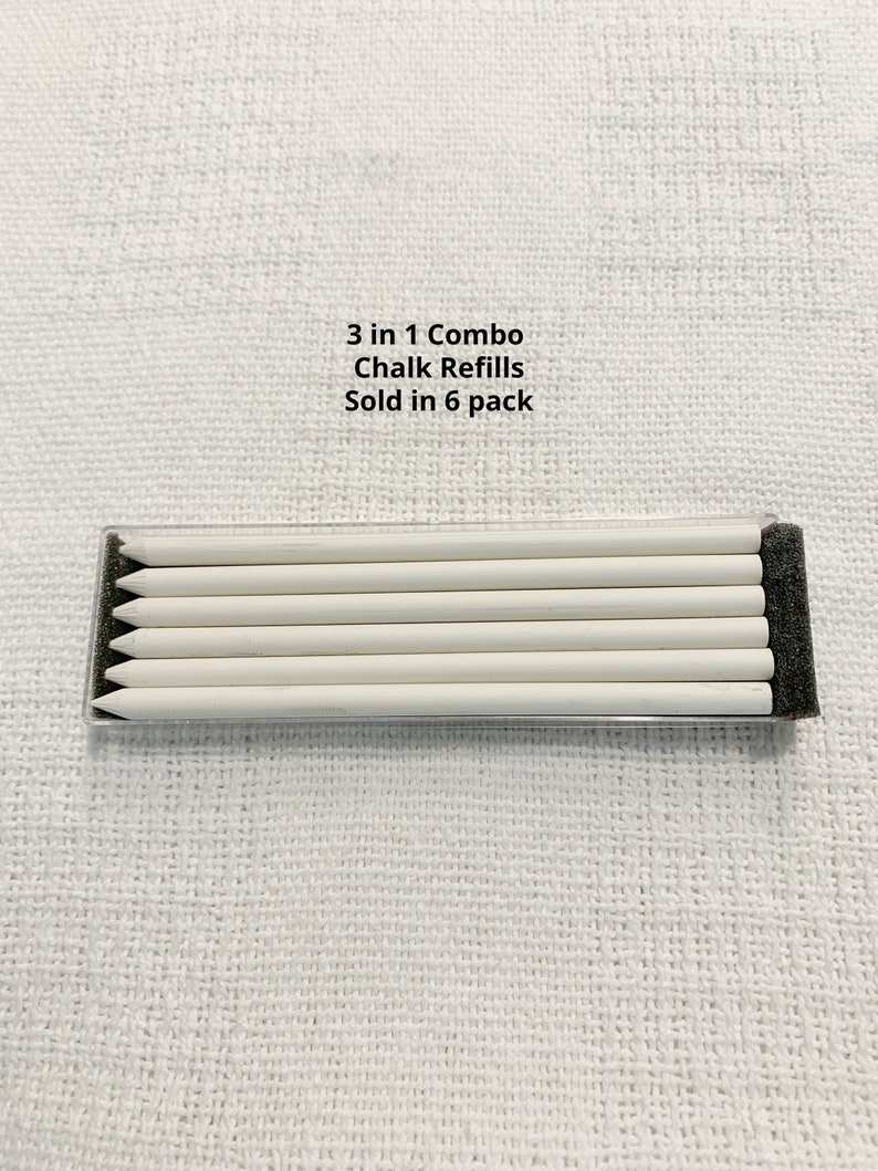 May include: A set of six white chalk refills arranged horizontally in a clear plastic case with black foam ends. The text 3 in 1 Combo Chalk Refills Sold in 6 pack is printed above the container. The chalk sticks are cylindrical and pointed.