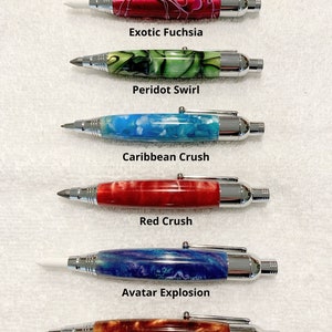 May include: Six 3 in 1 marking tools with chrome hardware and marbled resin barrels in various colors labeled Exotic Fuchsia, Peridot Swirl, Caribbean Crush, Red Crush, Avatar Explosion, and Copper Crush, each featuring a distinct tip.