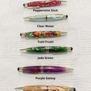 May include: Six pens with gold-tone accents and stylus tips, labeled Peppermint Stick, Clear Water, Tutti Frutti, Jade Green, Purple Galaxy, and Spalted Oak. Each pen features a unique barrel pattern, including red, blue, multi-color, green, purple, and wood grain designs. Text states: All pens are the same size.