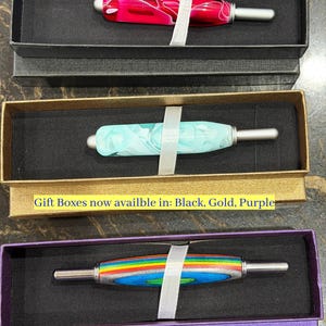 May include: Three seam rippers with decorative handles in black, gold, and purple gift boxes. The top handle is pink and white swirl, the middle is light blue and white swirl, and the bottom is rainbow striped. Text reads: Gift Boxes now availble in: Black, Gold, Purple.