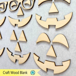 K&ouml;nnte beinhalten: Holzzuschnitte f&uuml;r Halloween-Bastelarbeiten. Das Bild zeigt verschiedene ausgeschnittene Formen von K&uuml;rbisgesichtern, einschlie&szlig;lich Augen, Nasen und M&uuml;nder. Der Text "Craft Wood Blank" ist unten links sichtbar.