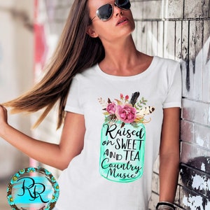 May include: White t-shirt with a teal mason jar graphic featuring pink flowers and the text "Raised on Sweet and Tea Country Music".