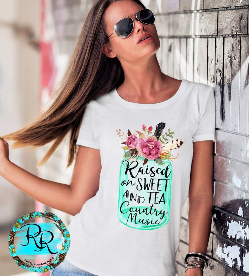 May include: White t-shirt with a teal mason jar graphic featuring pink flowers and the text "Raised on Sweet and Tea Country Music".