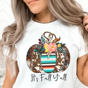 May include: White t-shirt with a brown, white, and turquoise pumpkin with floral accents. The text "It's Fall Y'all" is printed below the pumpkin.