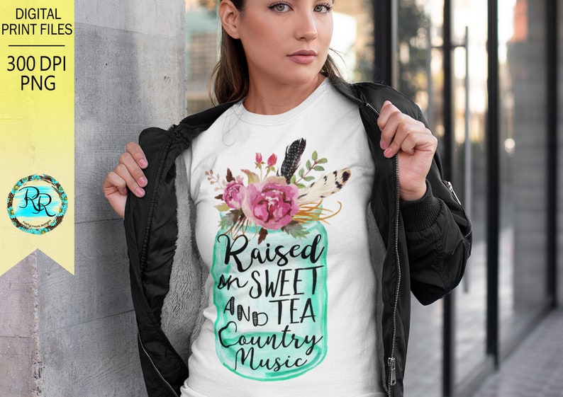 May include: White t-shirt with a teal mason jar graphic featuring flowers and feathers. The text on the jar reads "Raised on Sweet and Tea Country Music".