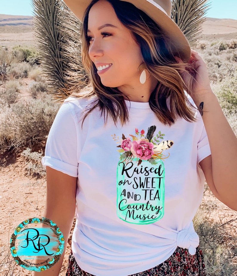 May include: White t-shirt with a teal mason jar graphic that says "Raised on Sweet and Tea Country Music". The jar is decorated with pink flowers and feathers.
