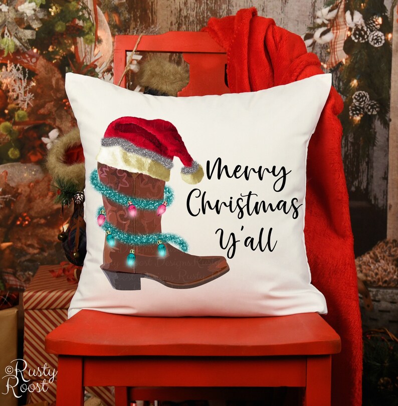 K&ouml;nnte beinhalten: Ein wei&szlig;es Kissen mit einem braunen Cowboy-Stiefel, der einen Weihnachtsmann-Hut tr&auml;gt und mit Weihnachtslichtern verziert ist. Der Text "Merry Christmas y'all" ist auf dem Kissen aufgedruckt.
